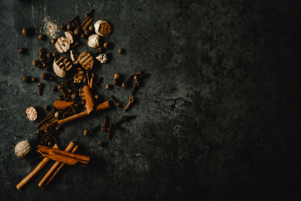 Whole Indonesian spices — cinnamon, clove and nutmeg — on a dark surface.